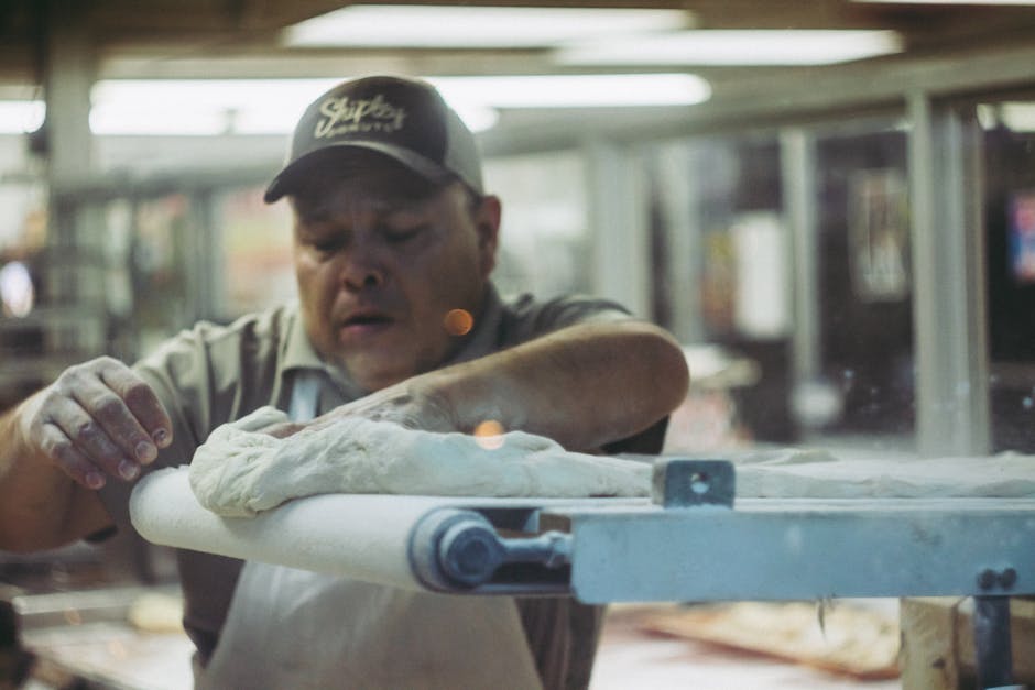 Male baker in a bakery shop preparing dough on a rolling machine indoors.
