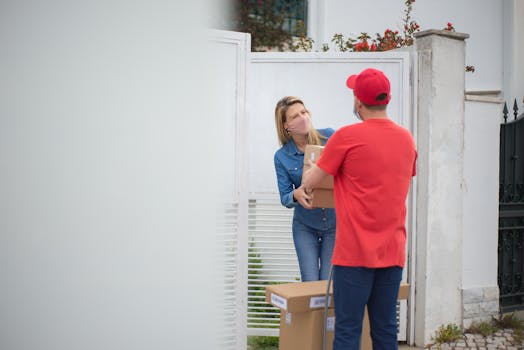 A delivery man hands a package to a woman at a metal gate, following COVID-19 precautions.